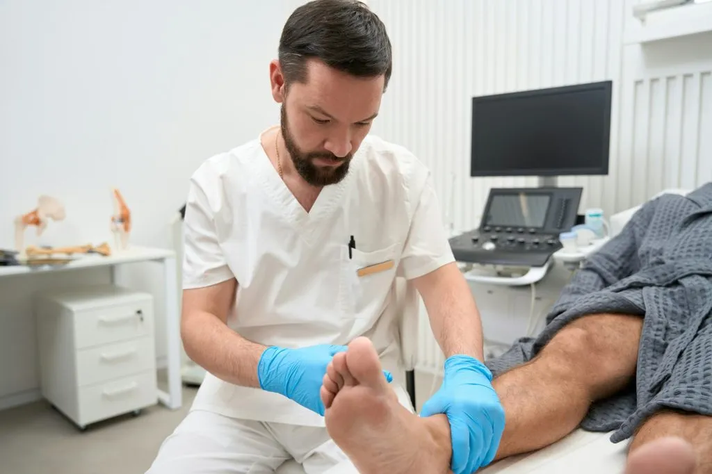concentrated male doctor performing an examination of man ankle